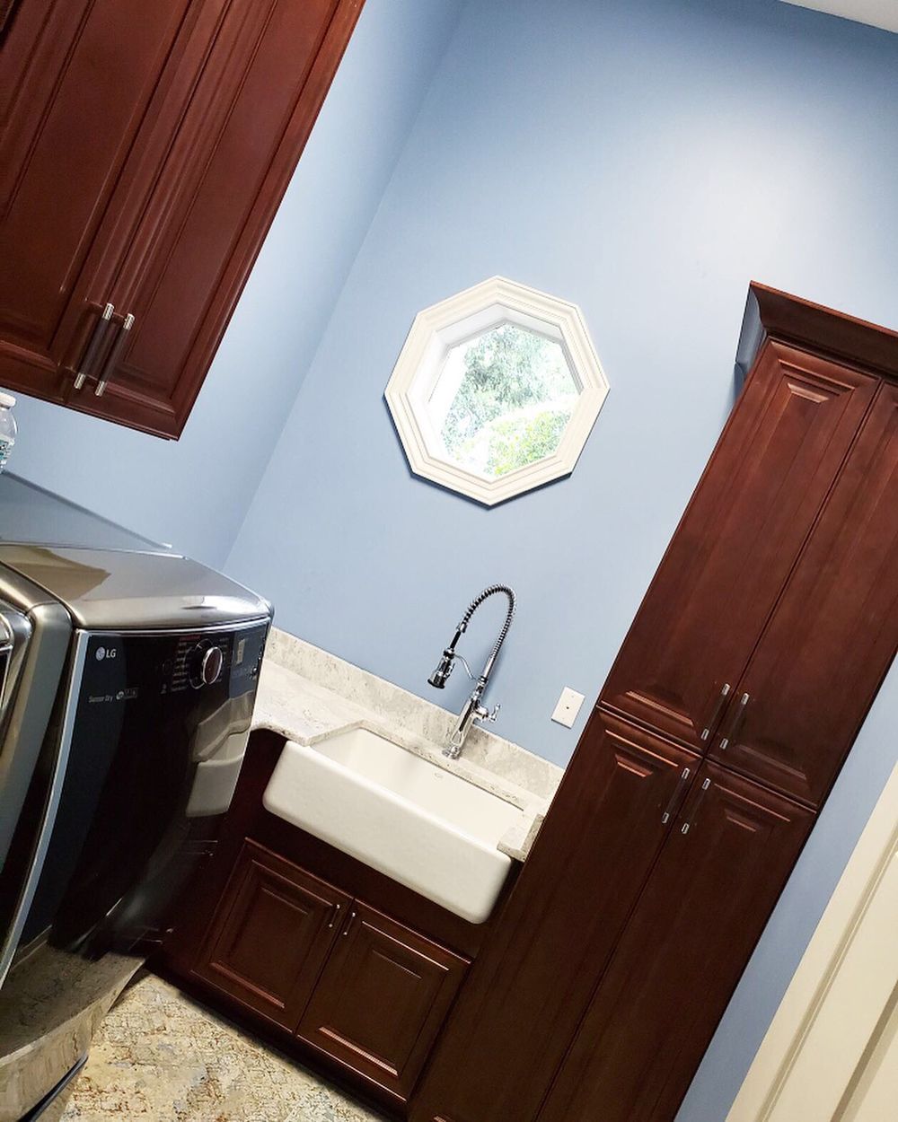 Laundry room with blue walls, brown cabinets, white sink, washer/dryer, and an octagonal window.