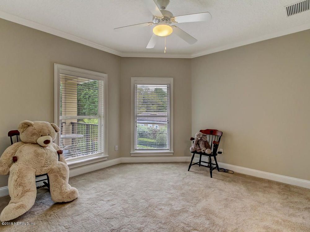 Empty beige room with carpet, teddy bear, chair, and windows.