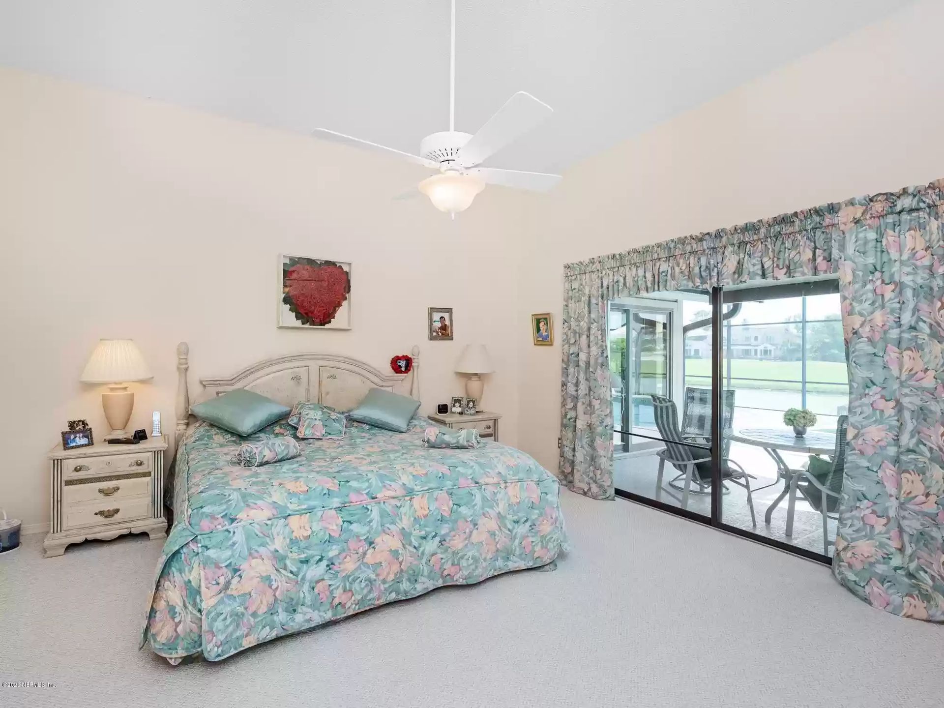 Bedroom with a floral bedspread, matching curtains, and a view of the patio through glass sliding doors.