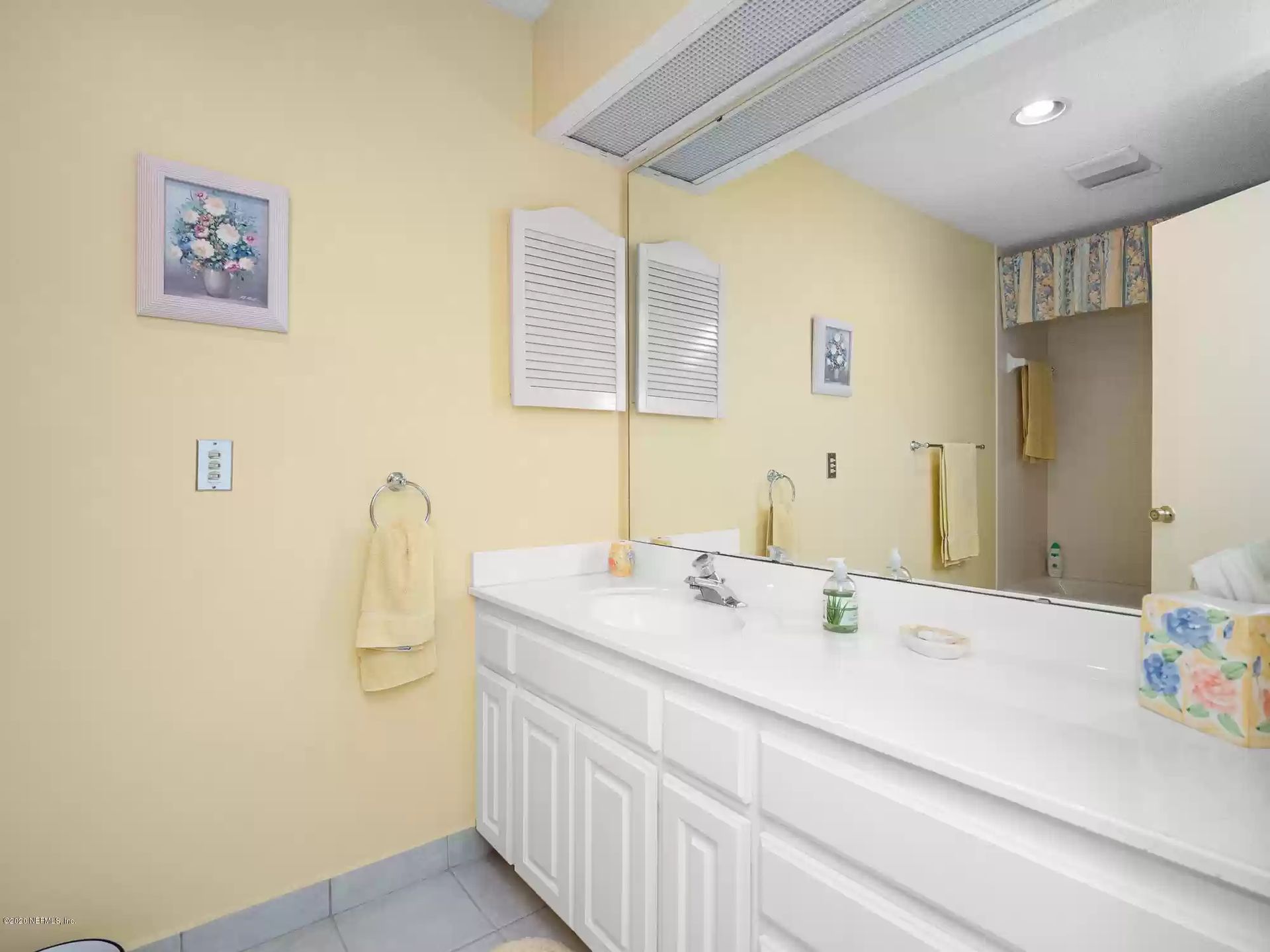 Bathroom with white vanity, yellow walls, blue floor, mirror, and accessories.