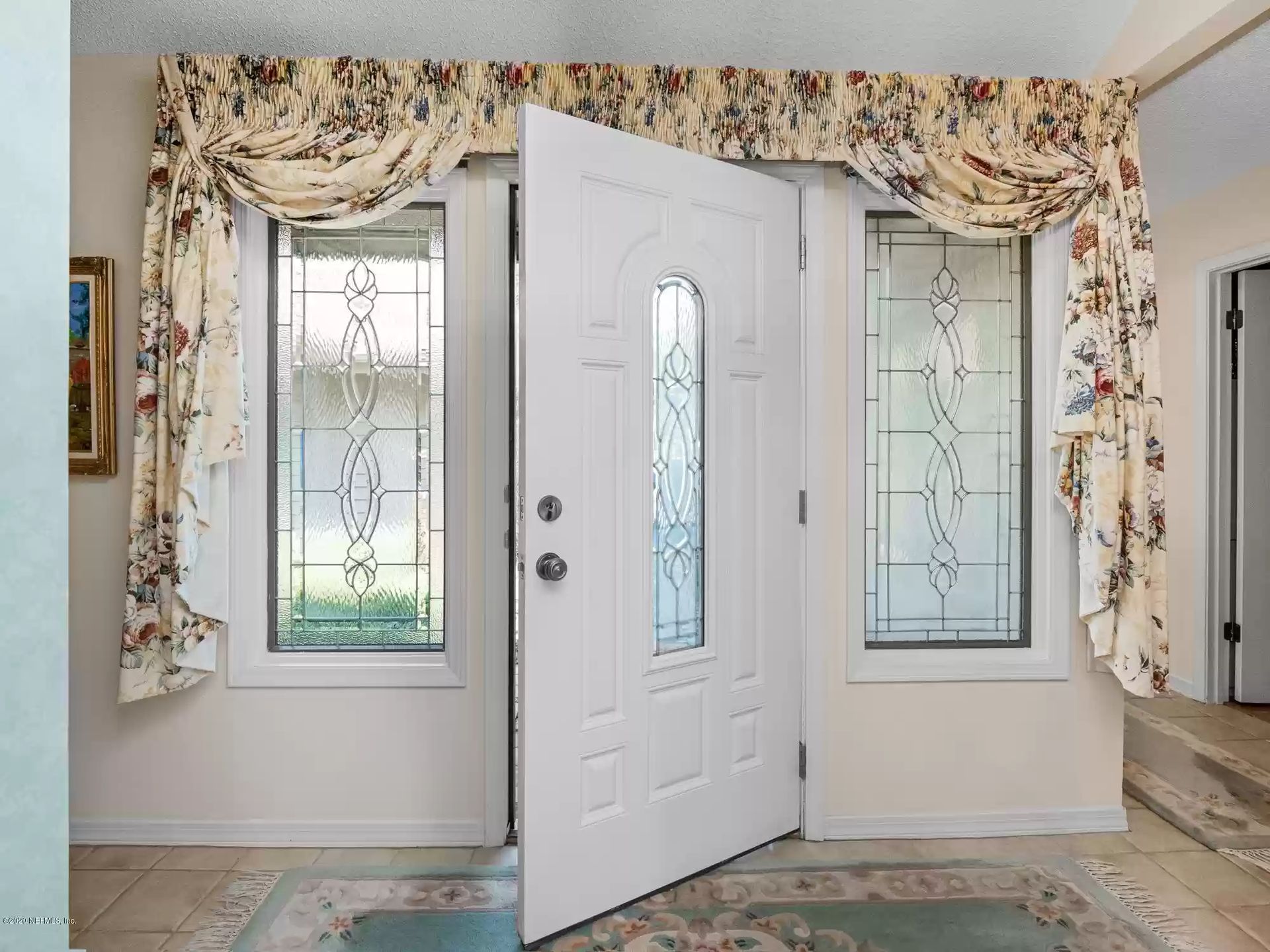 White front door open, flanked by windows with decorative glass, floral valance, beige tile floor.