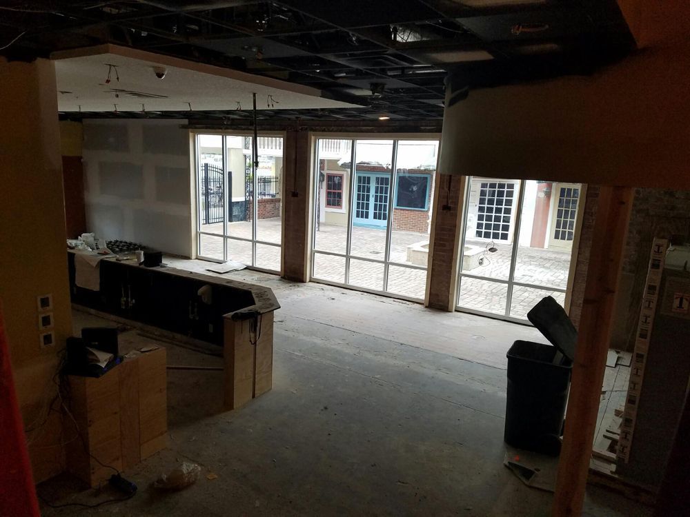 Interior view of a space under construction with large windows overlooking an outdoor area with blue doors.