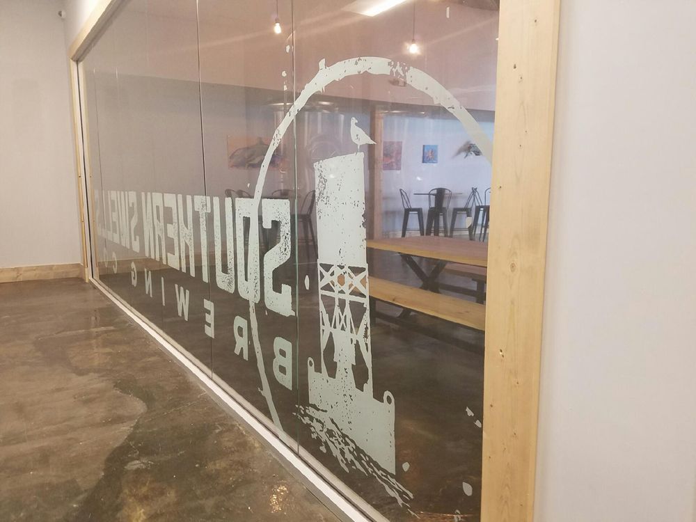 Interior window with etched Southern Tier Brewing logo, showing a glimpse of tables and chairs inside the brewery.