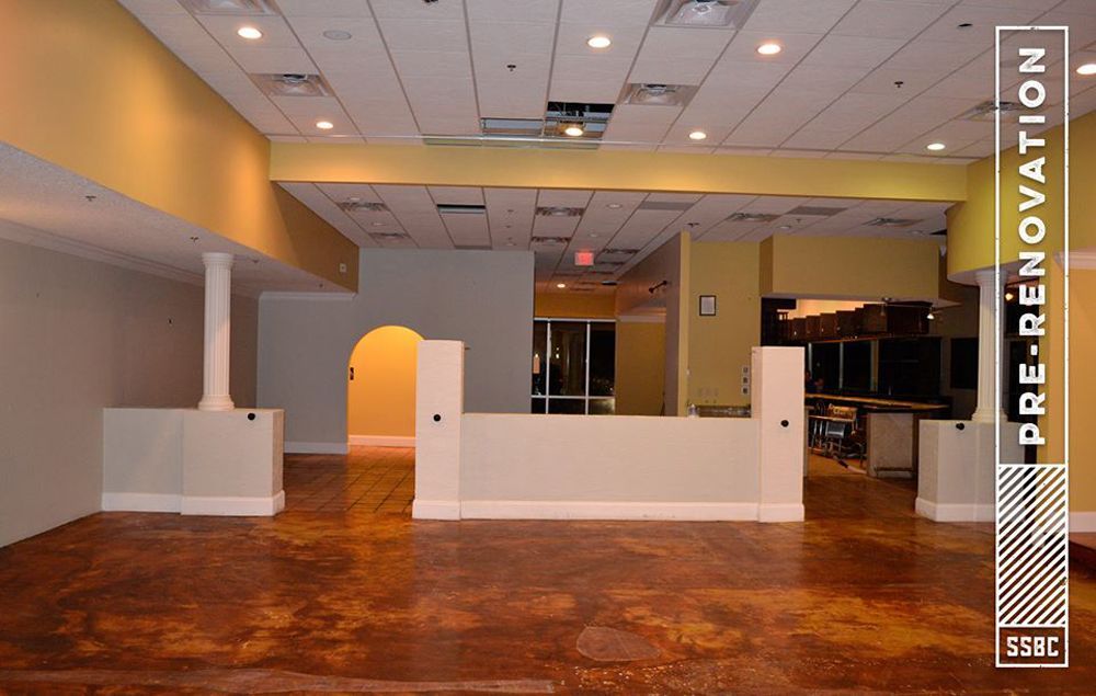 Empty commercial space, pre-renovation. Tan walls, brown floor, white pillars.