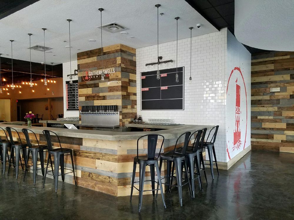 Bar interior with a concrete bar, black stools, and wood and white tile accents.