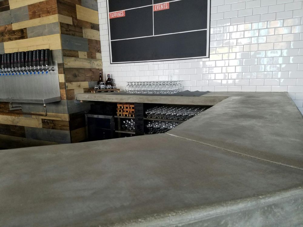 Interior view of a bar with a concrete counter, beer taps, and a chalkboard scoreboard.
