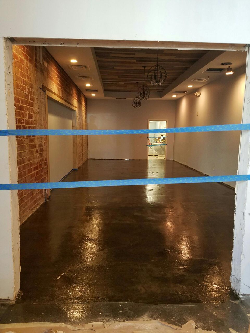 Empty room with glossy brown floor, exposed brick wall, and blue tape across doorway.