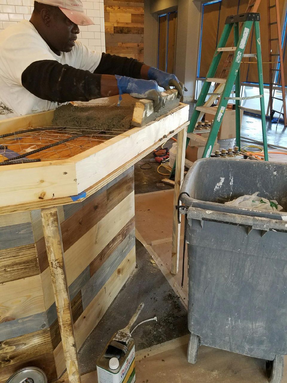 Person working on a wooden bar with concrete, a ladder, and a construction bucket.