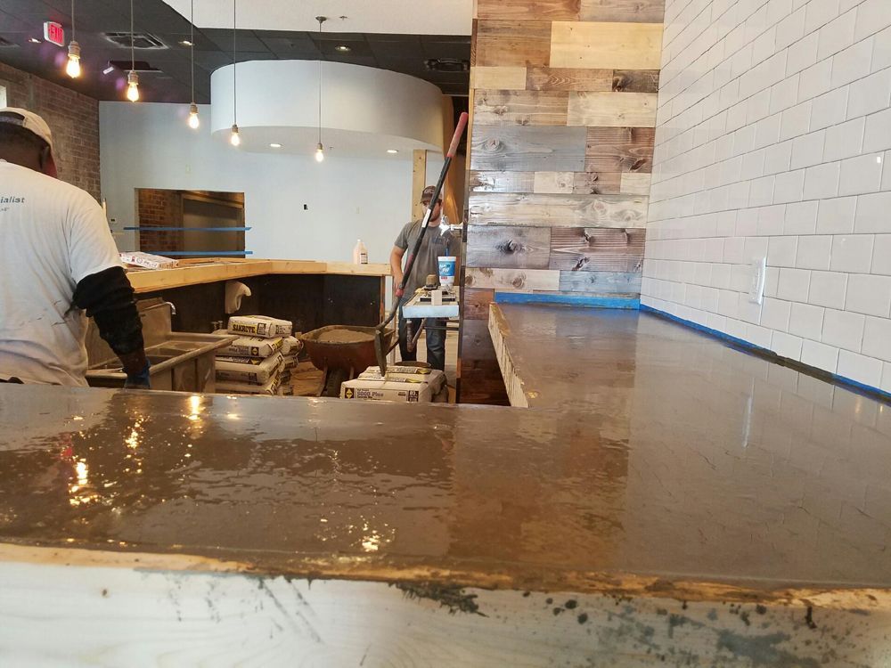 Construction workers installing a polished concrete countertop in a restaurant with exposed brick and wood accents.
