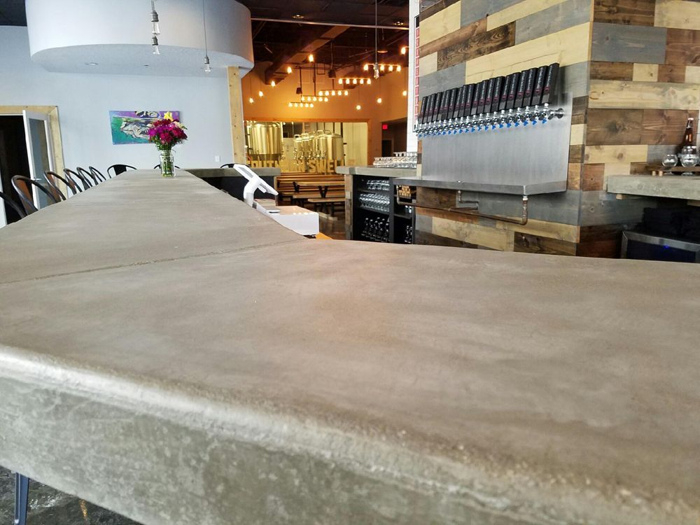 Bar with concrete counter, beer taps, and wooden wall. Inside a brewery.