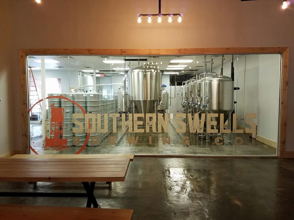 Southern Swells Brewing Co. with brewery equipment behind glass. Tables in foreground, orange logo visible.