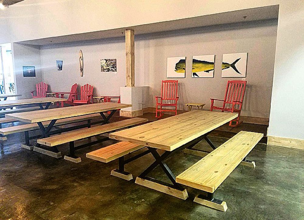Indoor seating area with picnic tables, benches, red rocking chairs, and fish art on the wall.