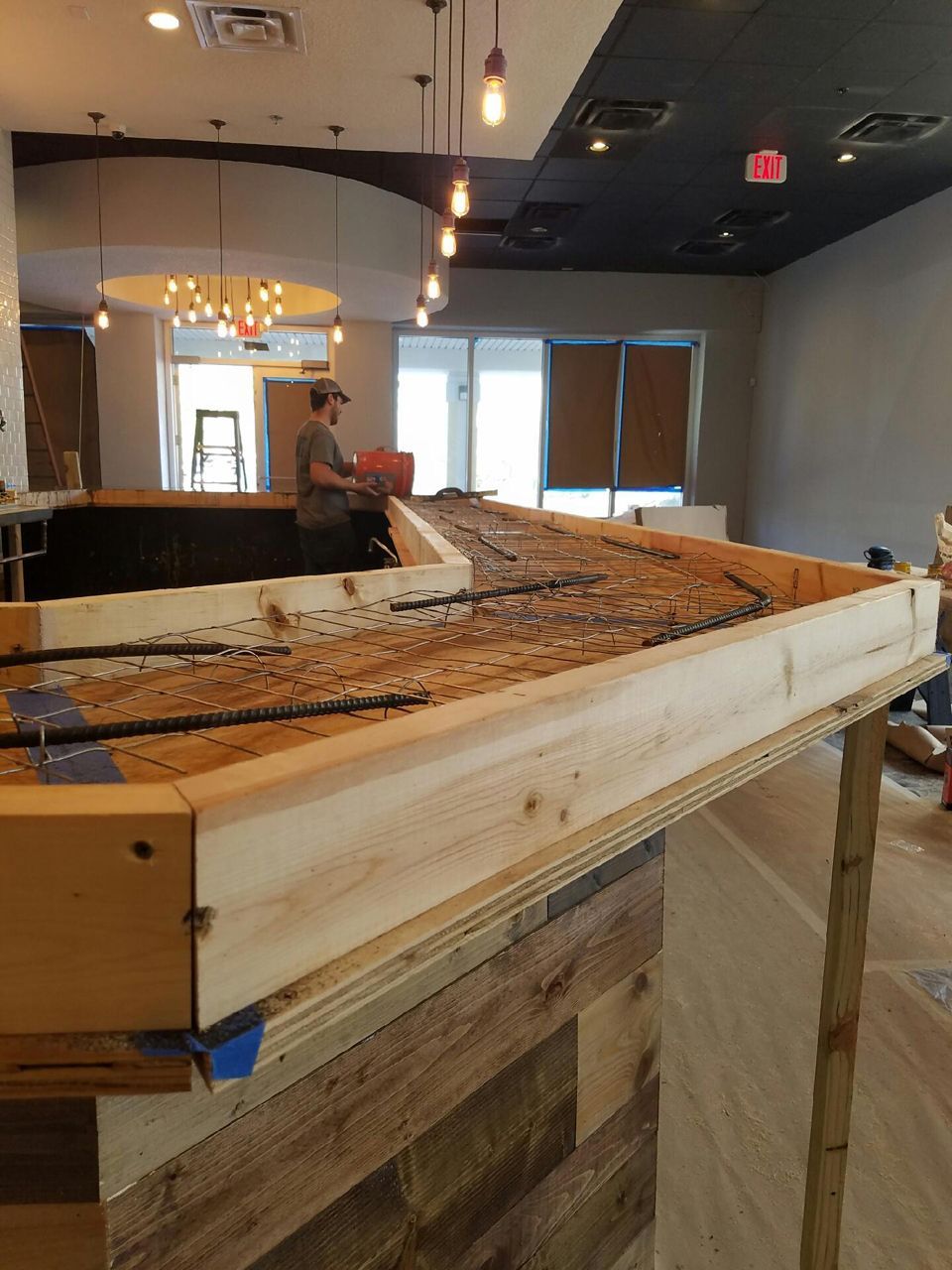 Bar under construction; worker adds concrete to a wooden form with exposed rebar.