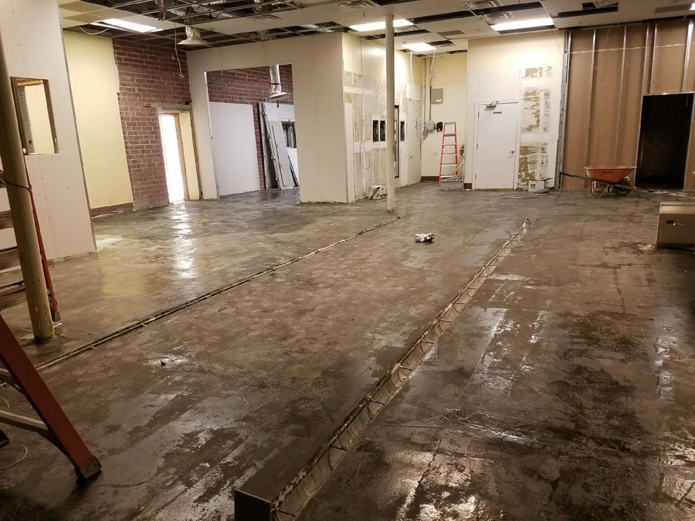 Interior space under renovation; concrete floor with long grooves, exposed walls.