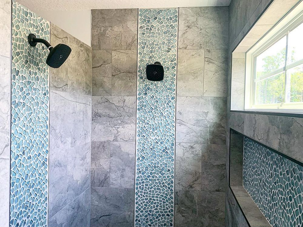 Shower with grey stone tiles, blue mosaic accents, black fixtures, and a window.