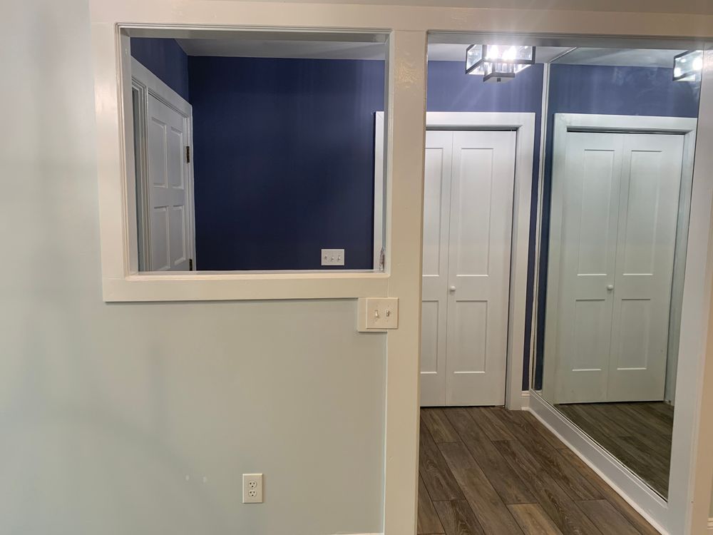 Interior with doorways, closets, blue and light blue walls, white trim, wooden floor.