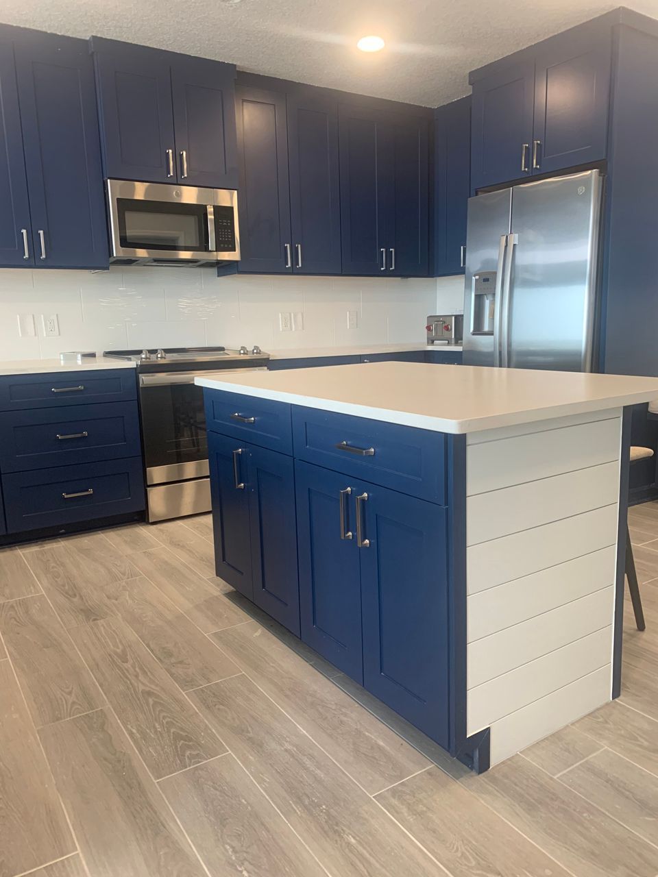 Navy blue kitchen cabinets with white countertops and island, stainless steel appliances.