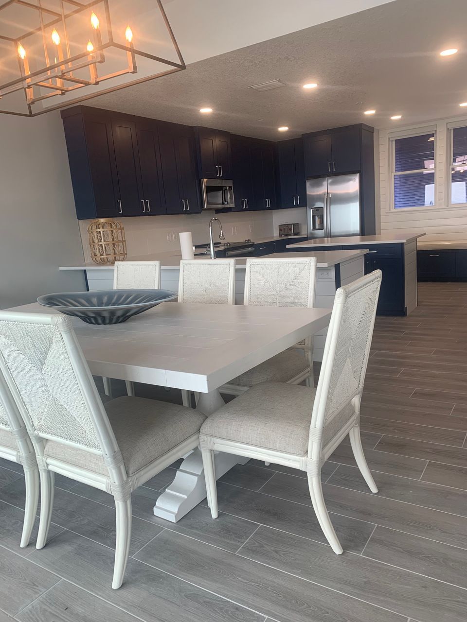 Open-concept dining room and kitchen with white table, blue cabinets, and gray flooring.
