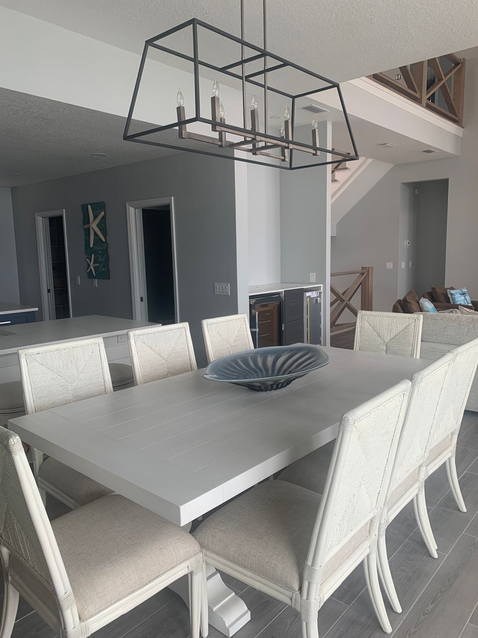 A modern dining room with a large table, chairs, and a geometric chandelier.