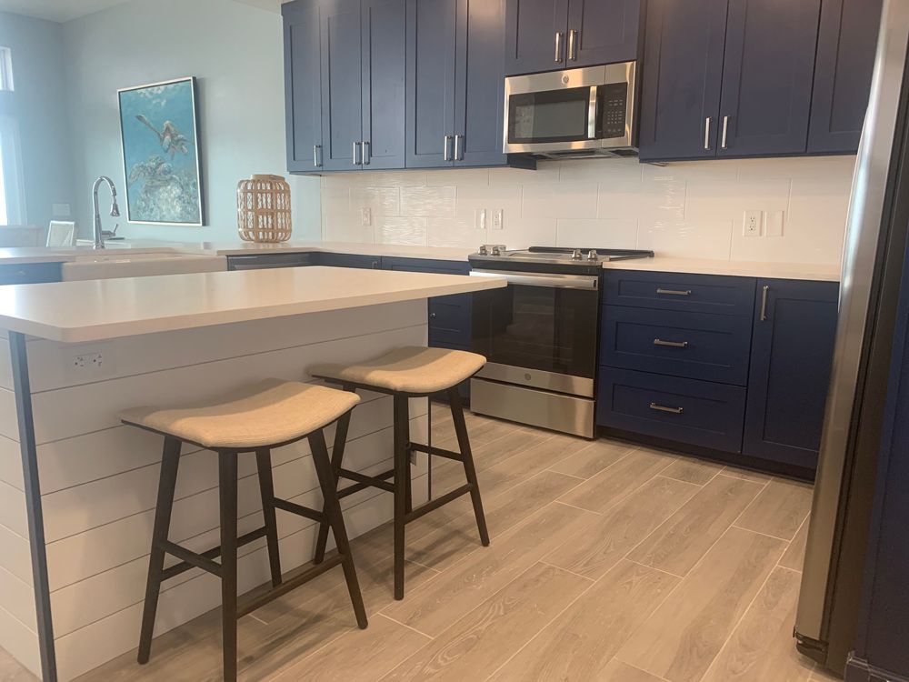 Modern kitchen with navy blue cabinets, white countertops, and two bar stools.