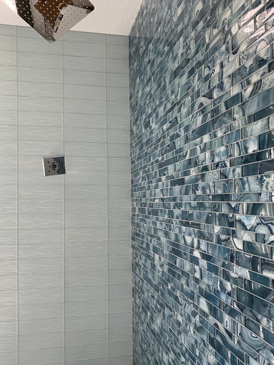 Shower with blue glass tile accent wall and light gray tile walls.