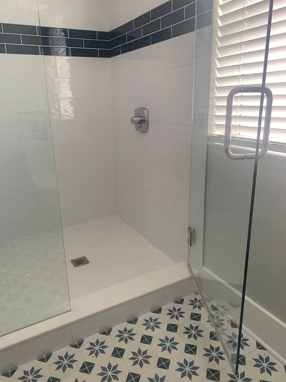 Shower with white tile walls, dark blue border, glass door, and patterned floor.