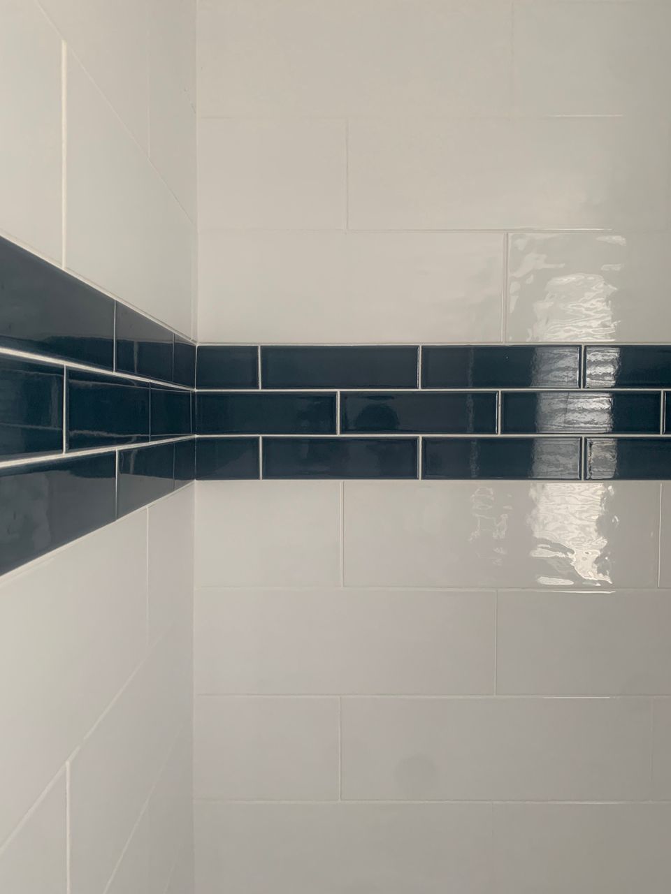 White tiled wall with a dark blue subway tile border in a corner.