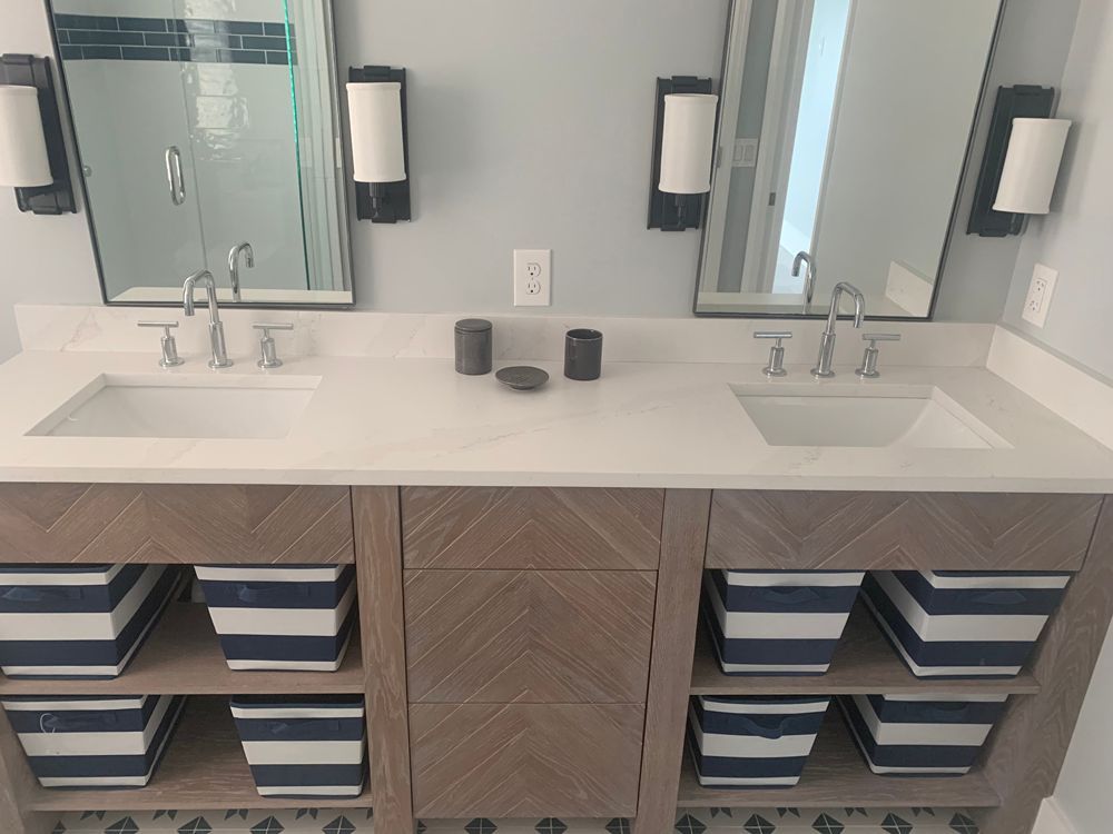 Bathroom with double sinks, mirrors, and wooden vanity with striped storage bins.