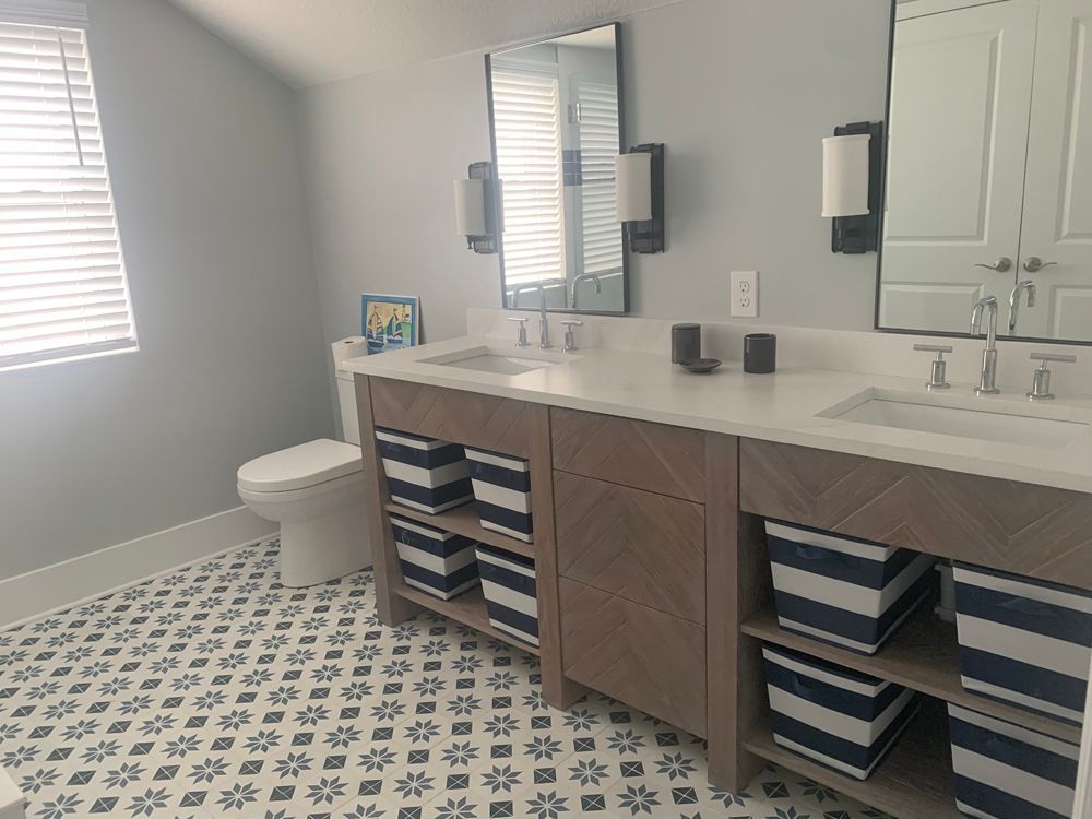 Bathroom with patterned tile floor, double vanity, and blue and white storage baskets.