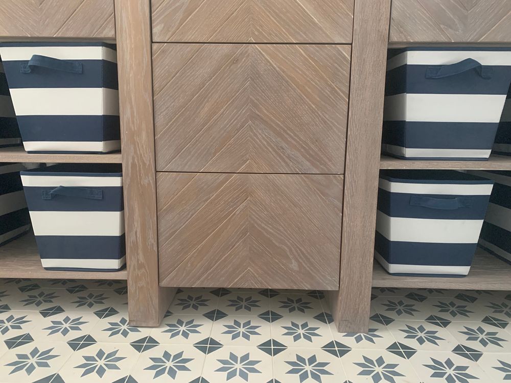 Wooden cabinet with navy and white striped storage bins on a patterned floor.