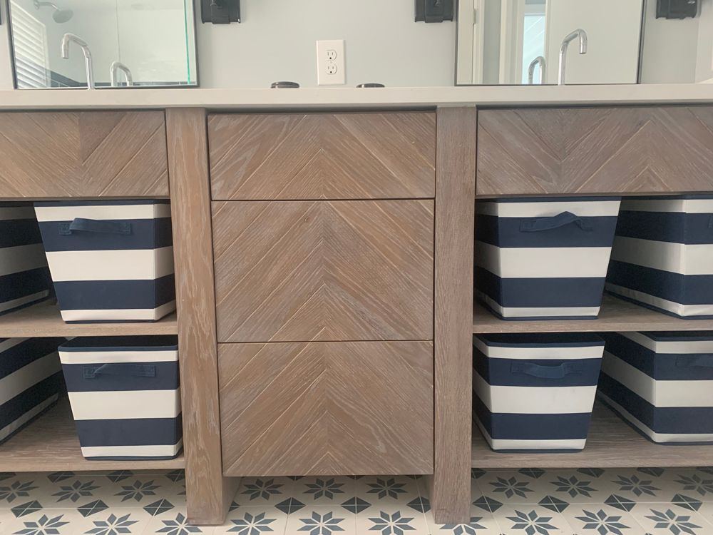Wooden bathroom vanity with drawers, open shelves, and blue-and-white striped storage bins.