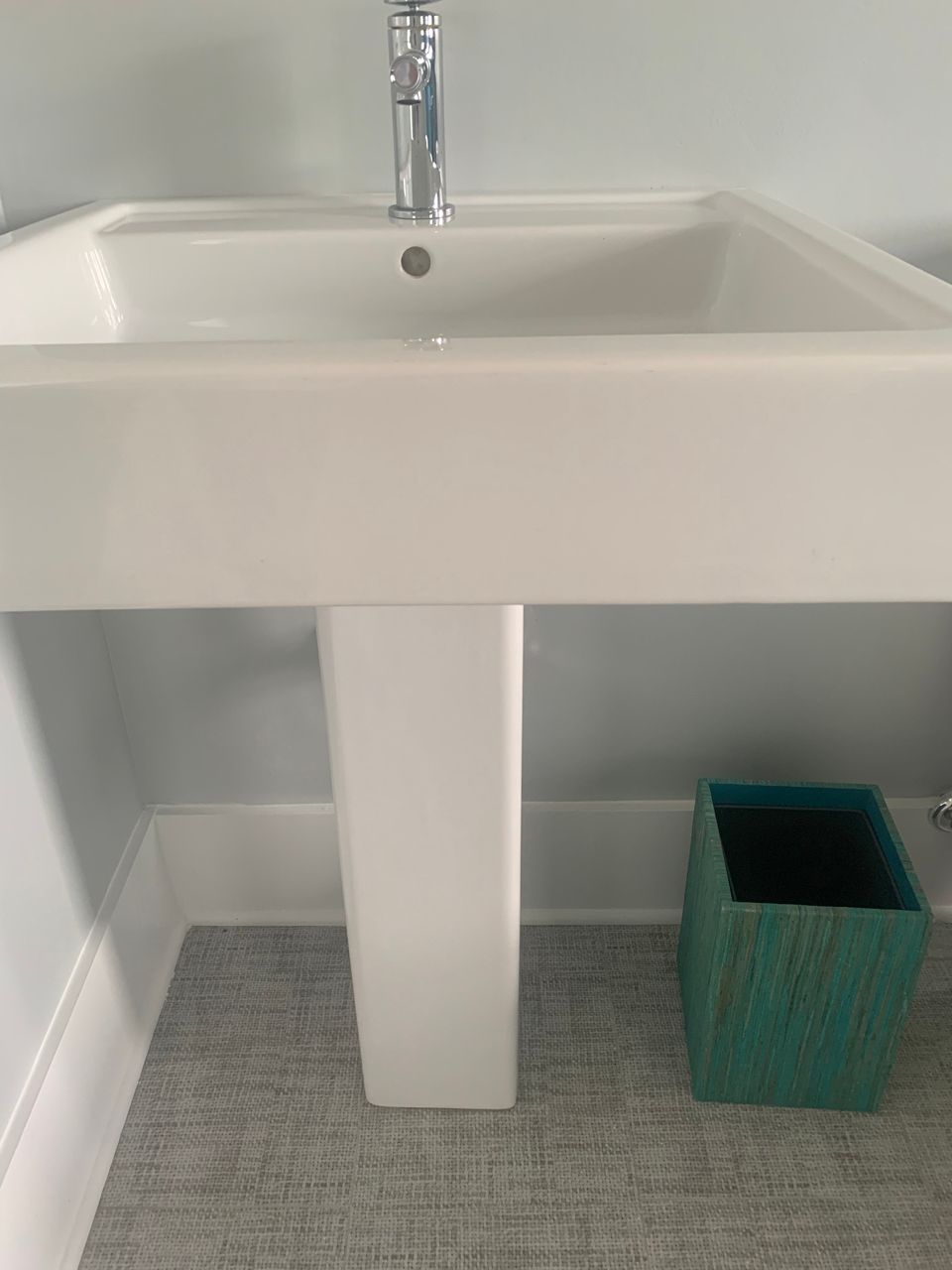 White pedestal sink in bathroom, turquoise trash can sits on floor.