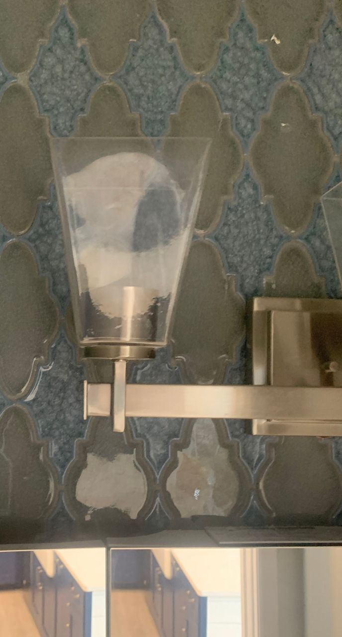 Brushed nickel vanity light with clear glass shade on blue patterned tile backsplash.