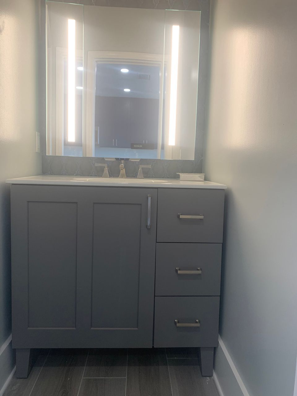 Gray bathroom vanity with countertop, mirror, and integrated lights.