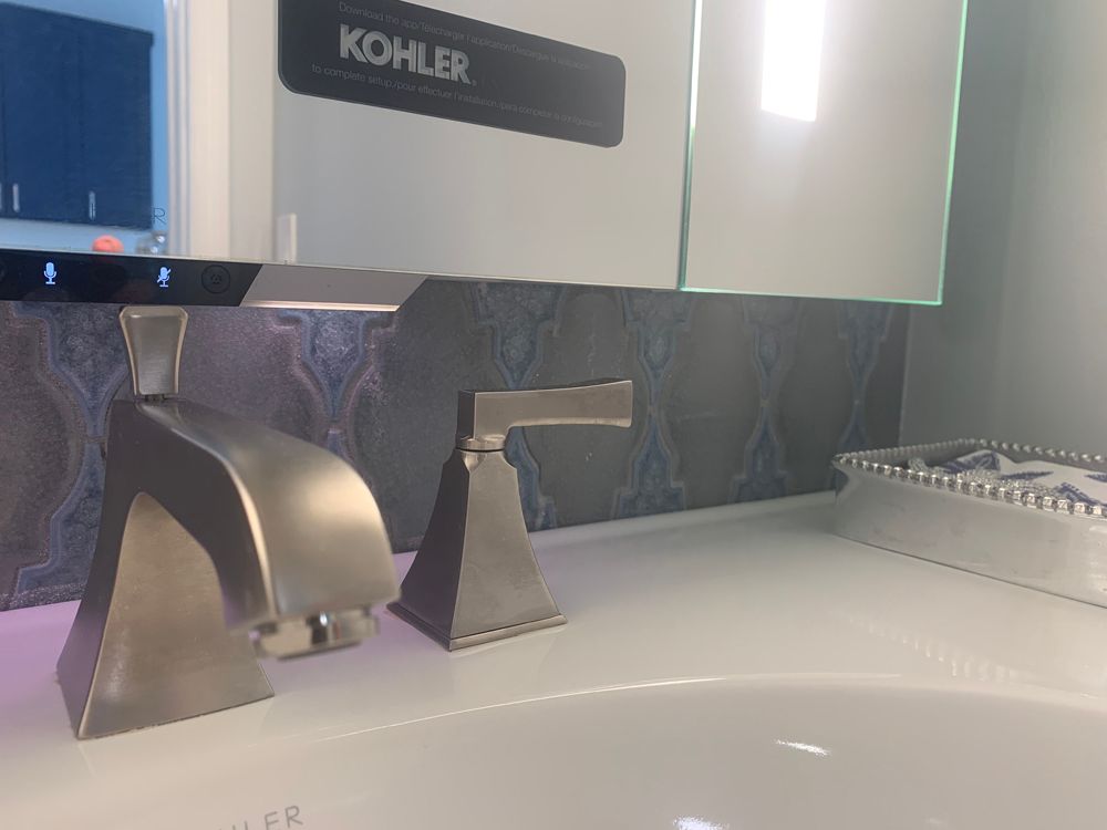 Close-up of a modern bathroom sink with silver fixtures, blue patterned backsplash, and Kohler logo.