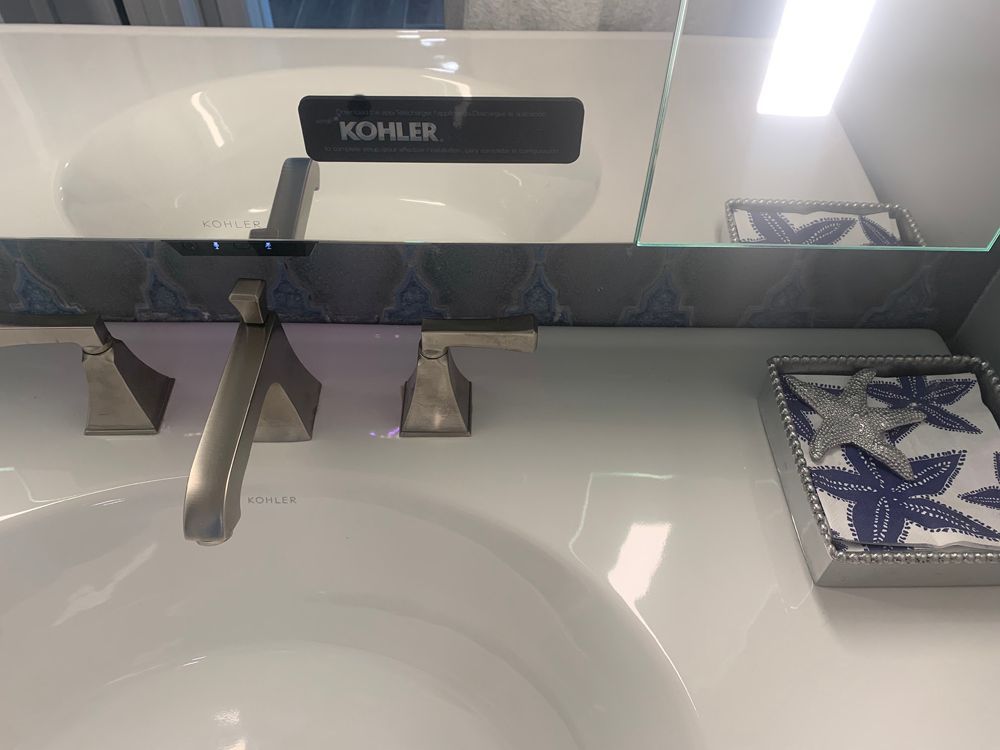 White bathroom sink with KOHLER faucet, floral patterned tray, and a partially visible mirror.