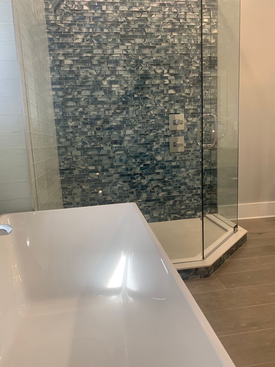 Shower with blue mosaic tile wall, glass doors, and a white sink in a modern bathroom.