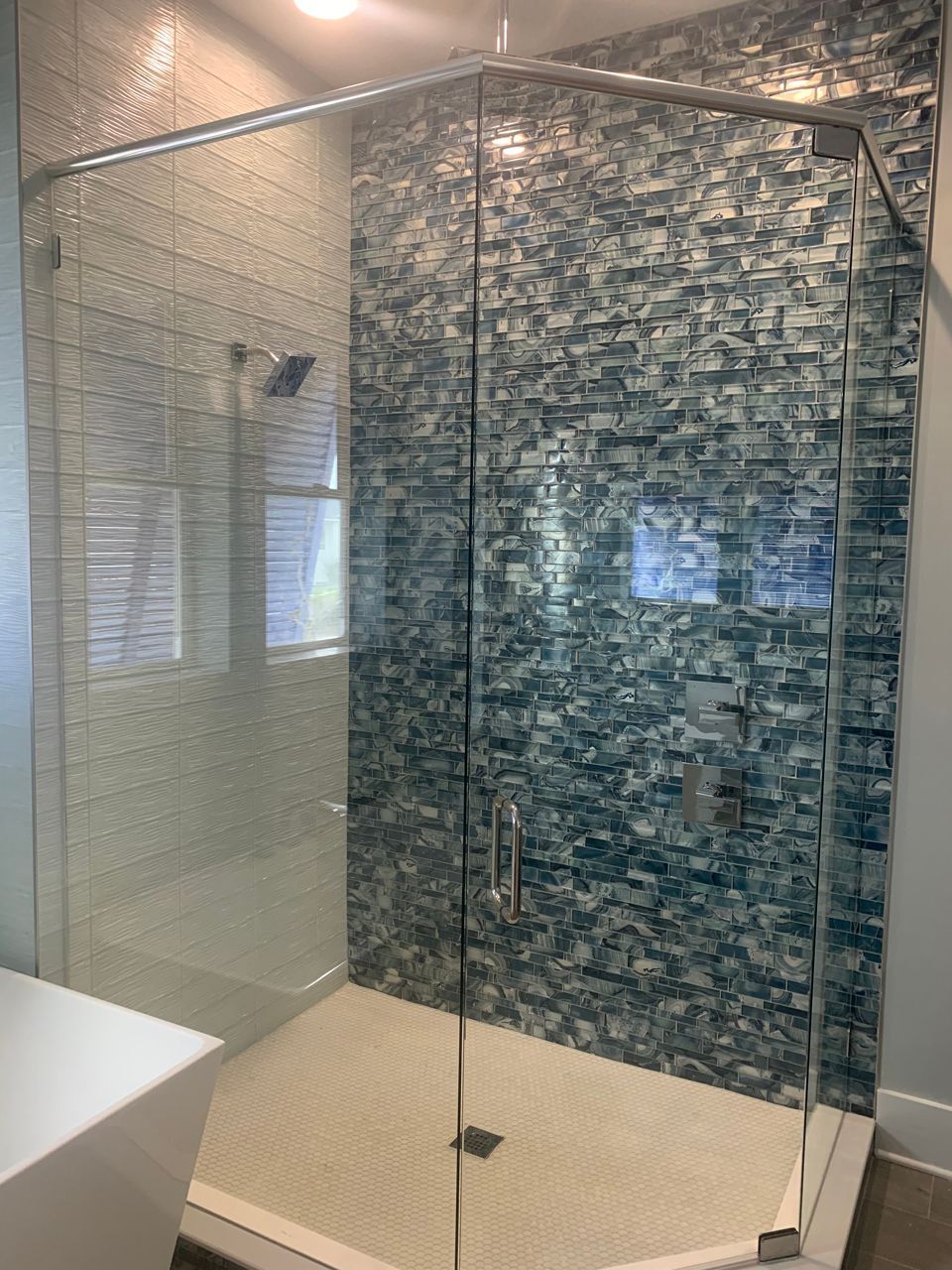 Glass shower enclosure with a blue tile accent wall and a white shower base.