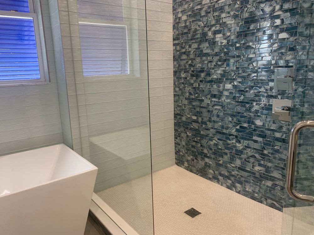 Bathroom with glass shower, blue mosaic tile wall, white tiled floor, and white freestanding tub.