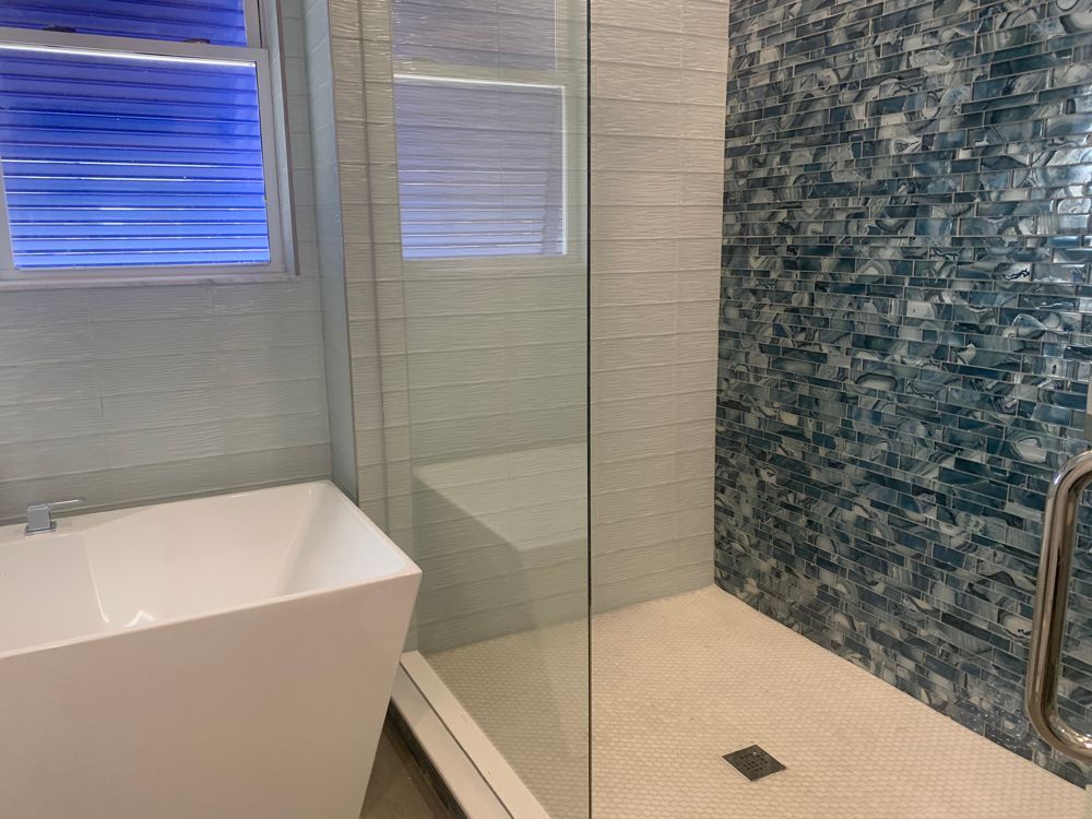 Modern bathroom with white tub, glass shower, and blue mosaic tile accent wall.