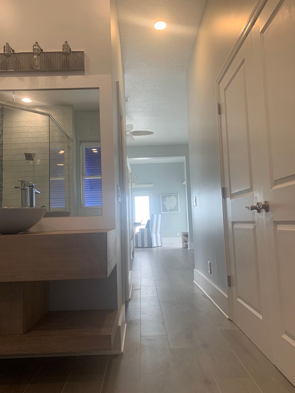Narrow hallway leading to an open space, with a bathroom on the left and a door on the right.