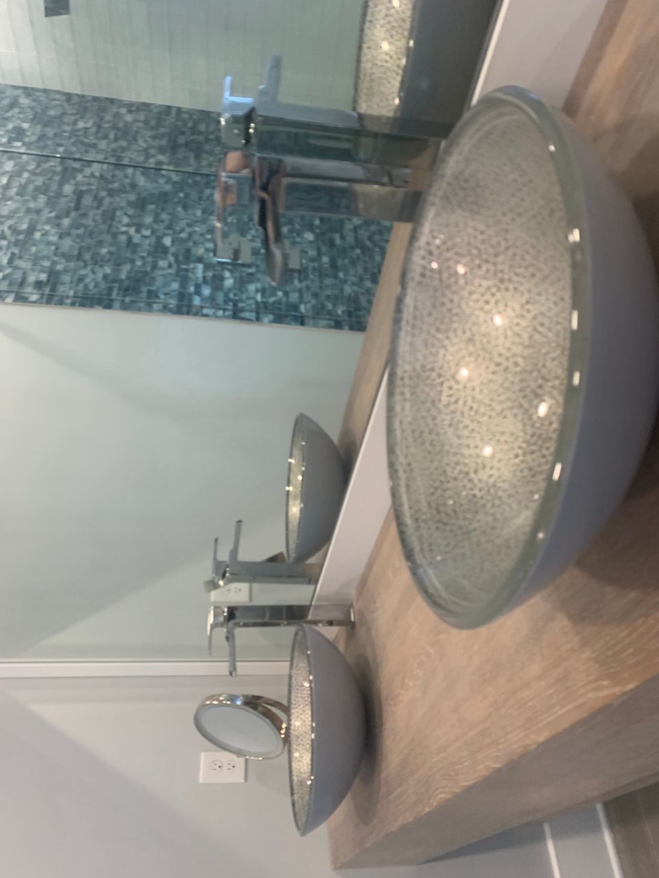 Modern bathroom with light blue vessel sinks on a wooden counter, a mirror, and textured wall tiles.