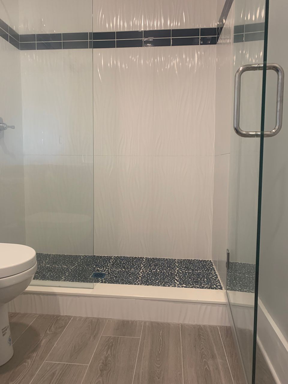 Bathroom shower with glass door, pebble floor, white walls, and dark blue tile trim.
