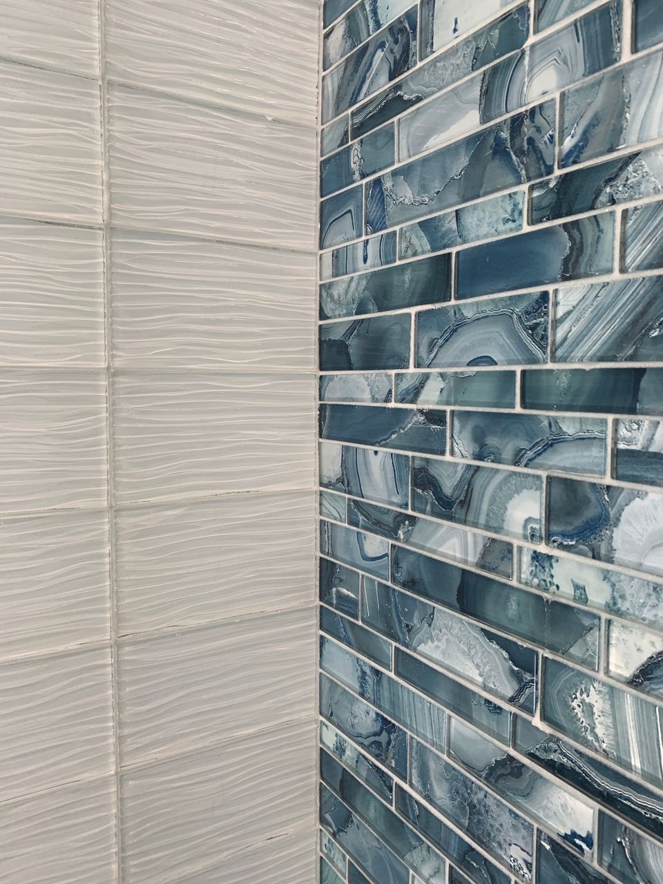 White textured tiles meet blue mosaic tiles at a corner.