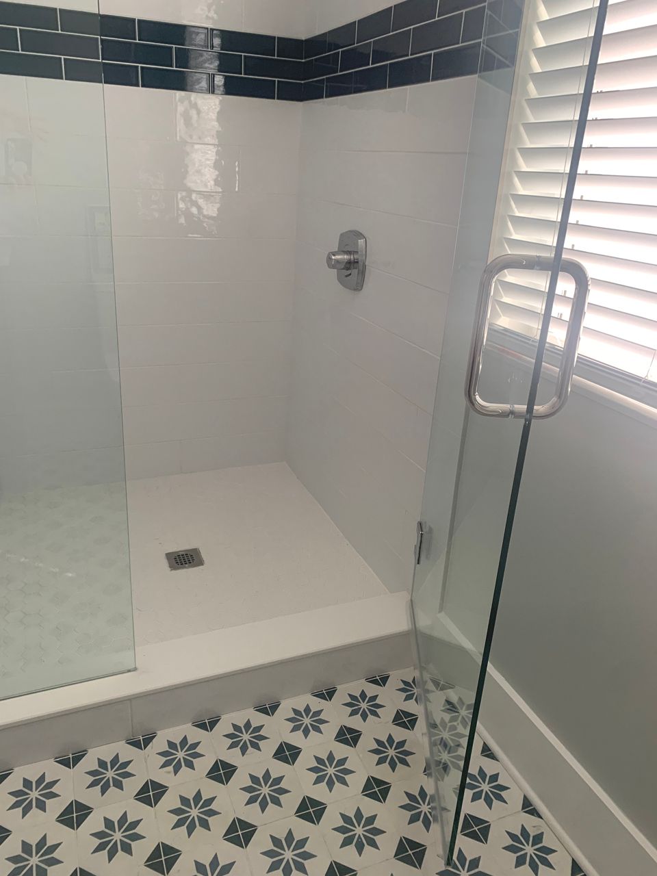 Walk-in shower with white walls, dark blue trim, glass door, and patterned tile floor.