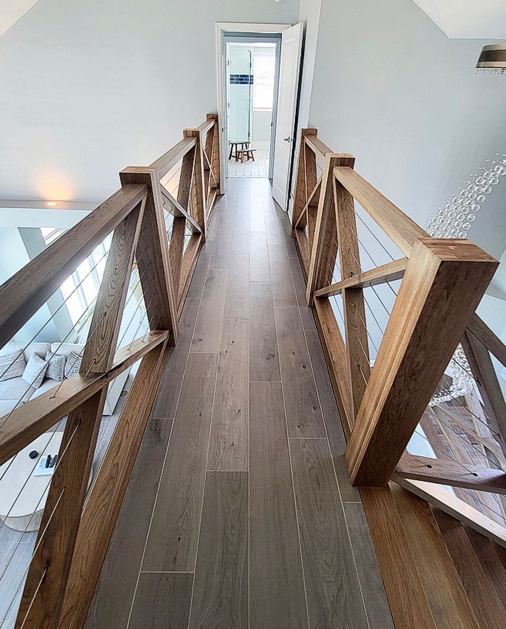 Wooden bridge with cable railings, gray wood flooring, leading to a doorway.