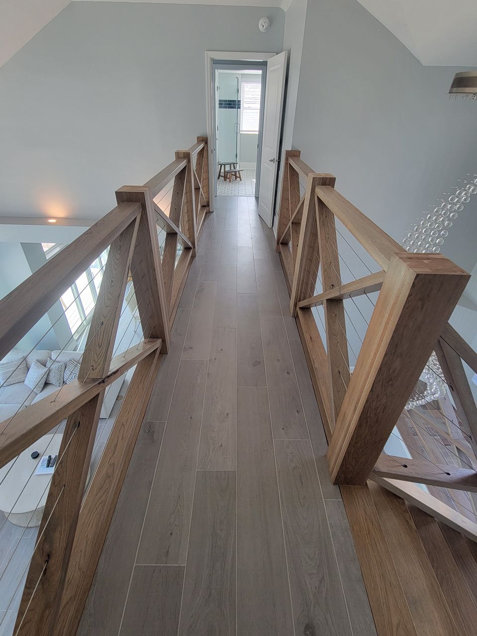 Wooden railing with cable accents lines a second-floor walkway overlooking a lower level.