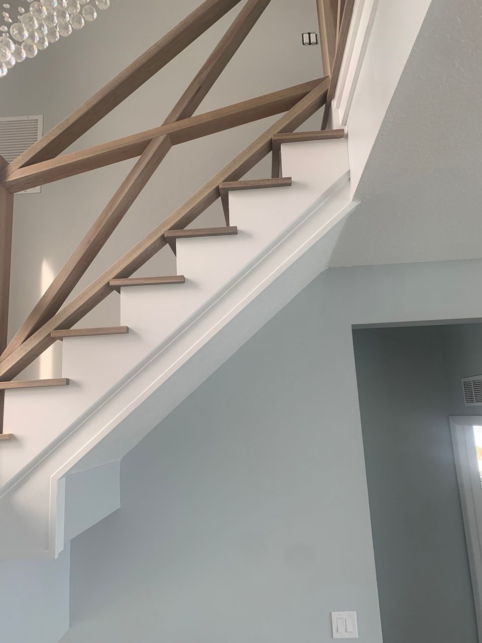 Staircase with white risers, gray treads, and wooden handrail against light blue wall.