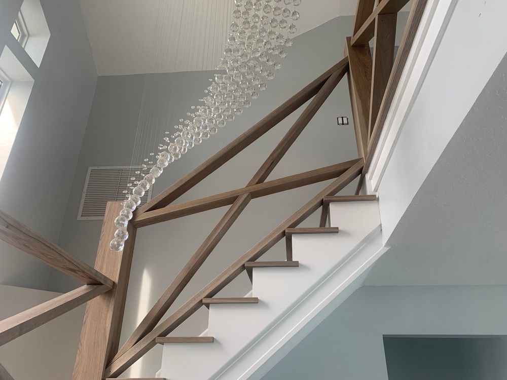 Wooden staircase with geometric railing, lit by a chandelier. Light blue walls.