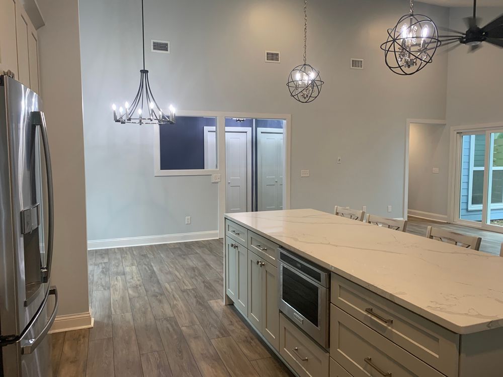 Kitchen with island, light wood floors, and pendant lights, including a window into a hallway with doors.